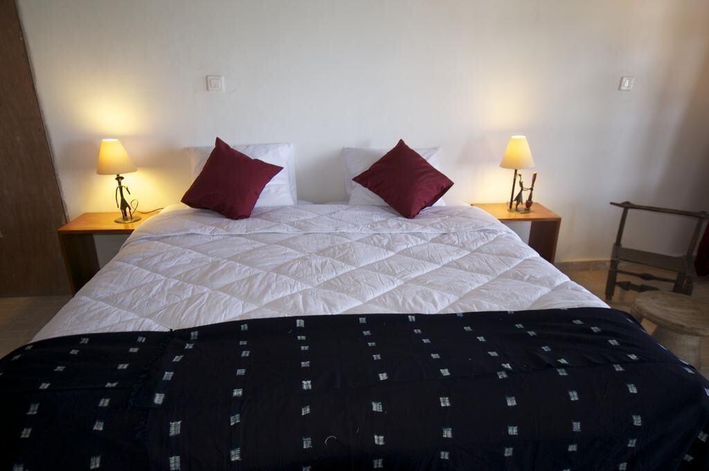 A neatly made bed with a white quilt and two red pillows, flanked by two bedside tables with lamps.