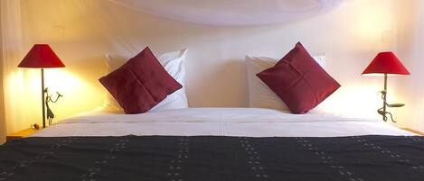 A bed with white linens and red pillows, two red lamps on either side, and a black bedspread with a pattern.