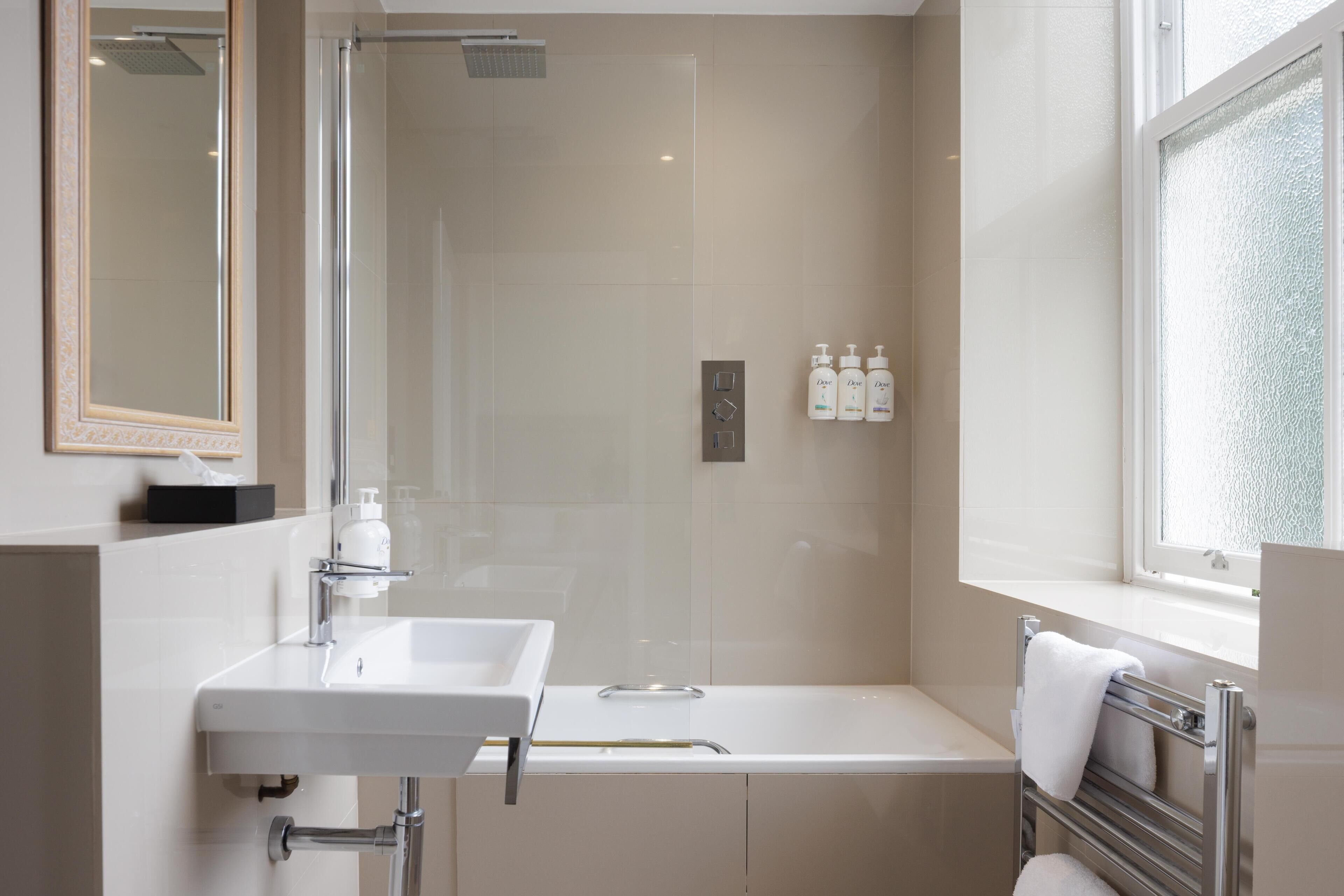 Ein modernes Badezimmer mit Waschbecken, Spiegel, Dusche und Badewanne. An der Wand befinden sich zwei Lotionflaschen.