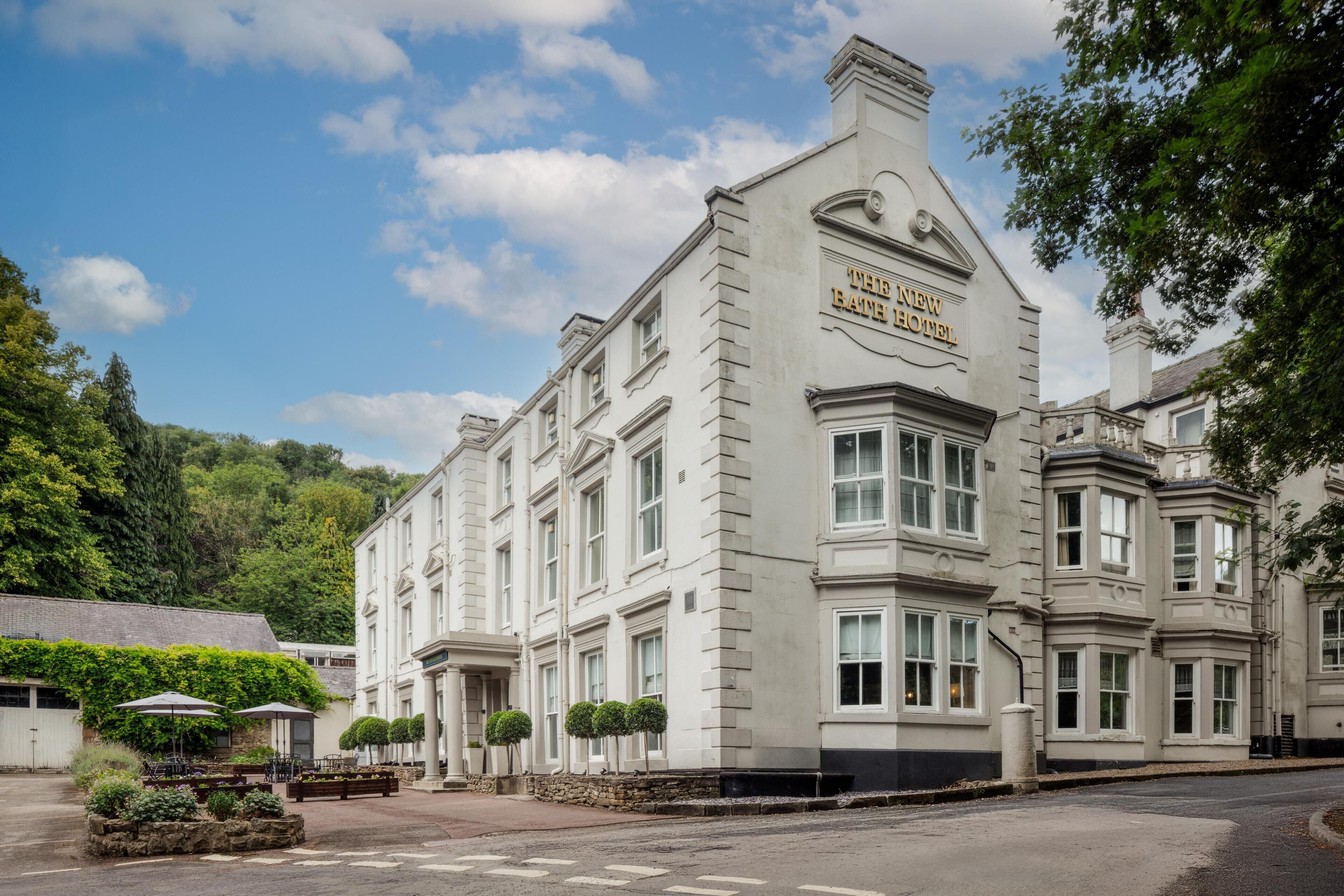 A large, historic building with a prominent sign reading "The New Bath Hotel." It features a symmetrical facade with multiple windows and a central entrance.