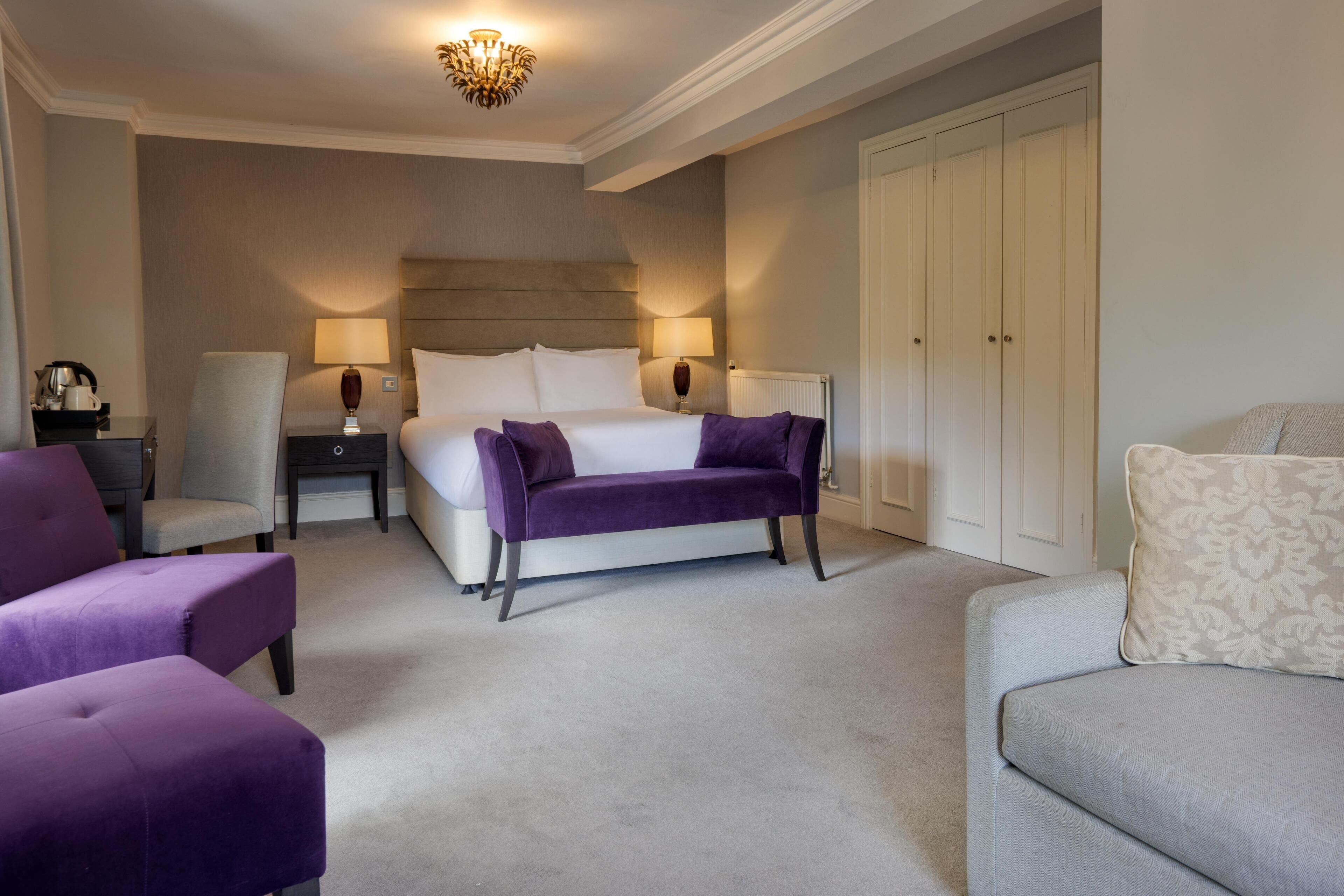 A hotel room with a large bed, two bedside tables, a nightstand, a chair, a sofa, and a wardrobe.