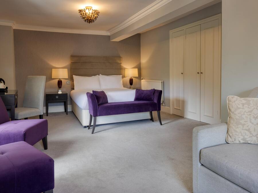 A hotel room with a large bed, two bedside tables, a nightstand, a chair, a sofa, and a wardrobe.