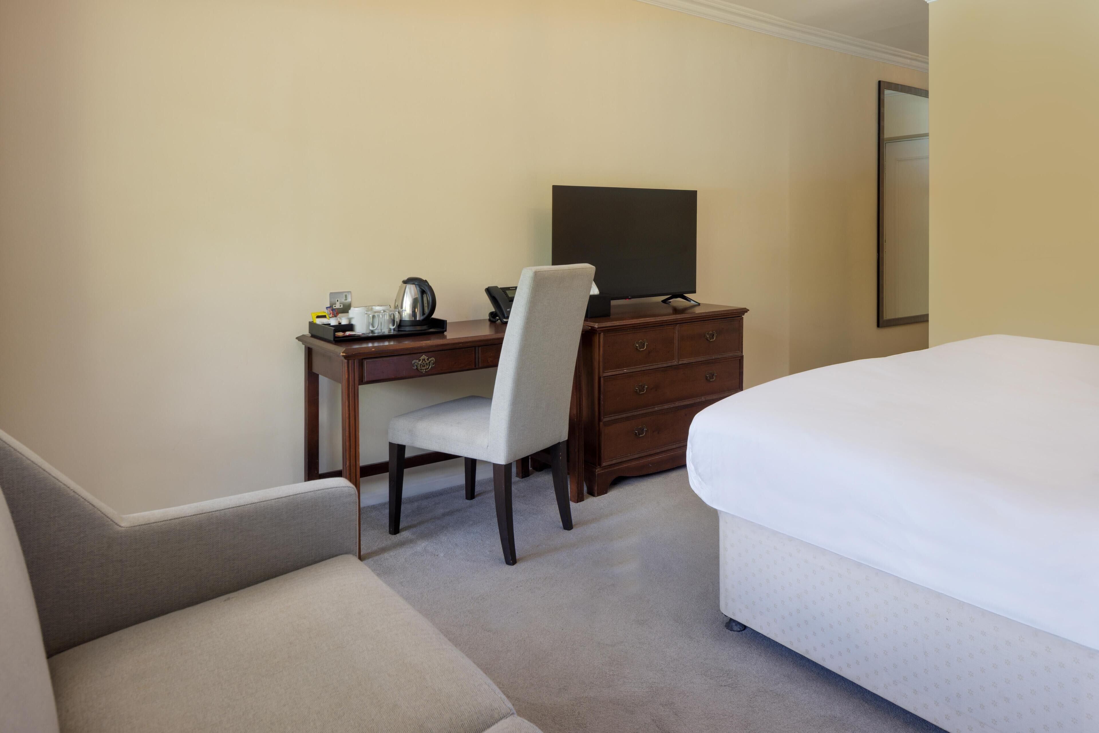 A hotel room with a bed, a desk with a chair, a television, and a dresser.
