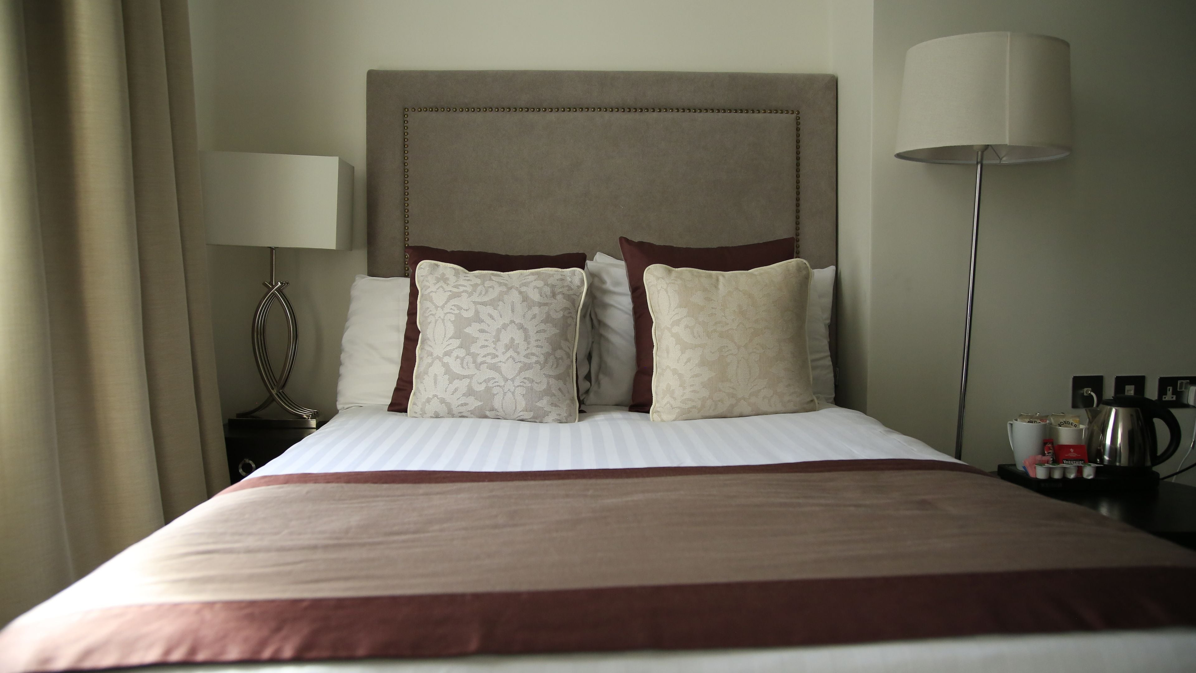 A neatly made bed with a striped bedspread, a headboard with a decorative pattern, and two bedside lamps.