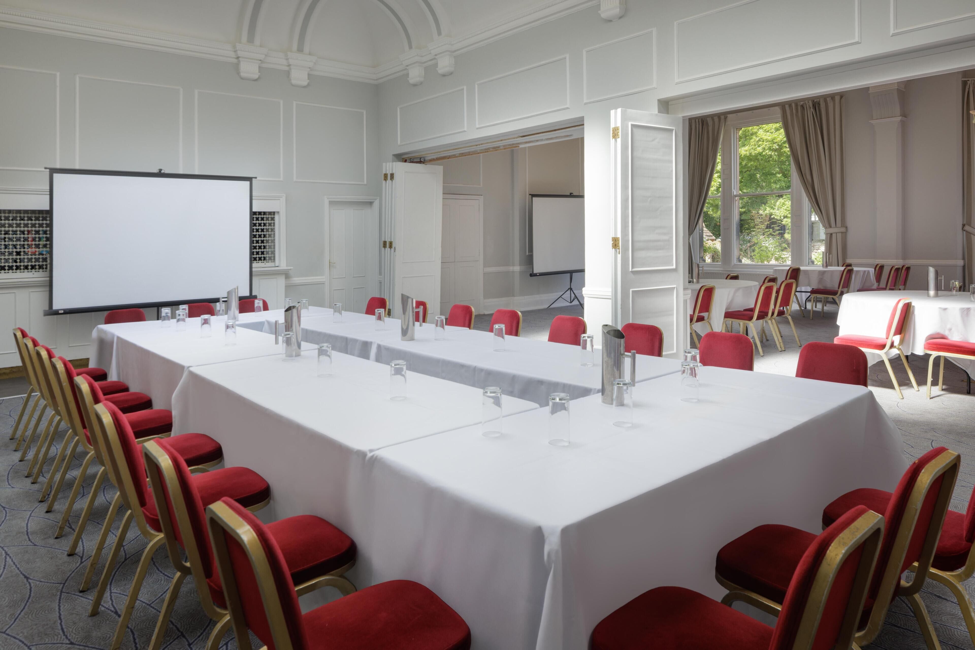 A conference room with a long table, red chairs, a projector screen, and a whiteboard.