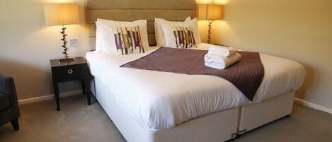 A neatly made bed with a brown throw blanket and white pillows, a bedside table with a lamp, and a headboard.