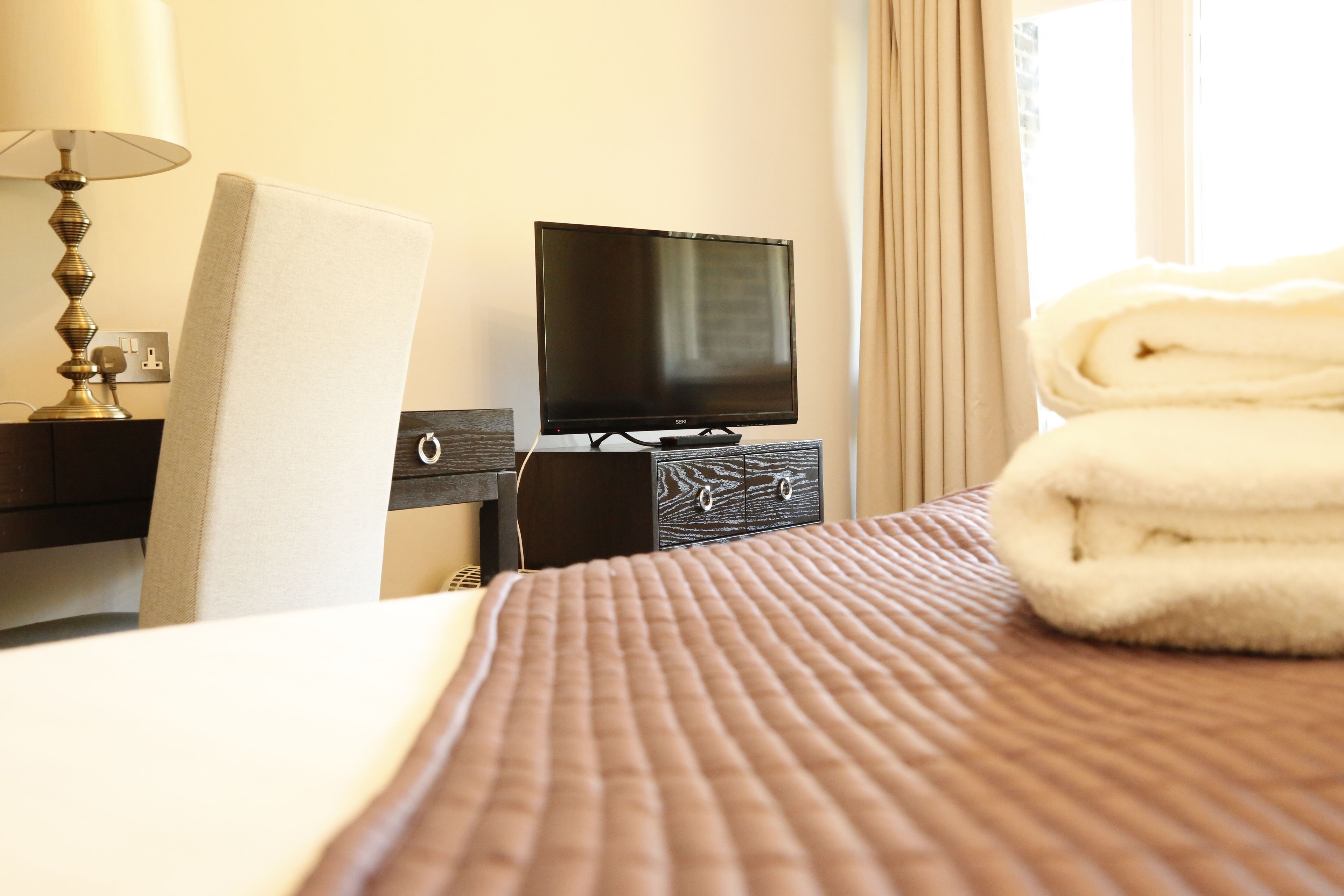 A hotel room with a bed, a television on a dresser, and a folded towel on the bed.