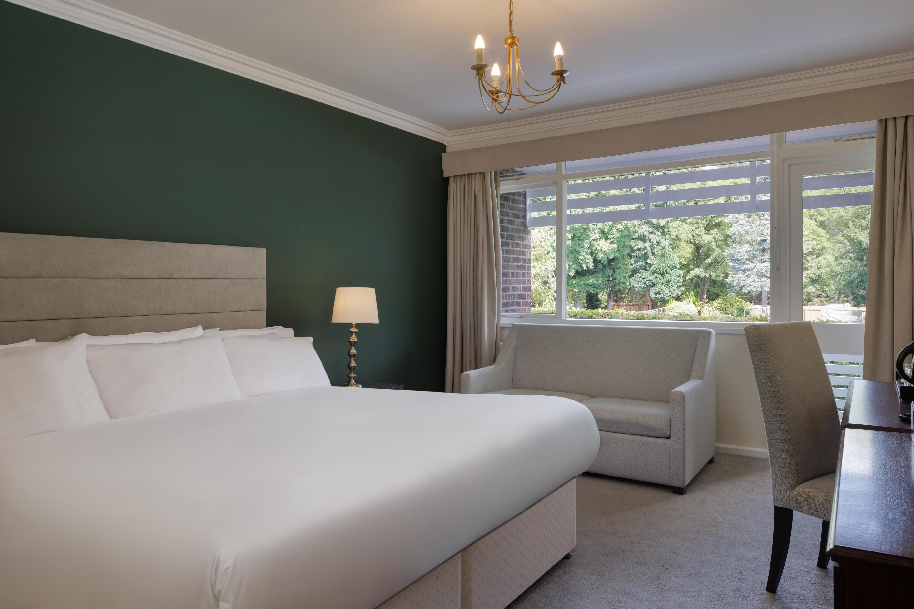 Une chambre d’hôtel avec un grand lit, un bureau, une chaise et une fenêtre donnant sur un paysage verdoyant.