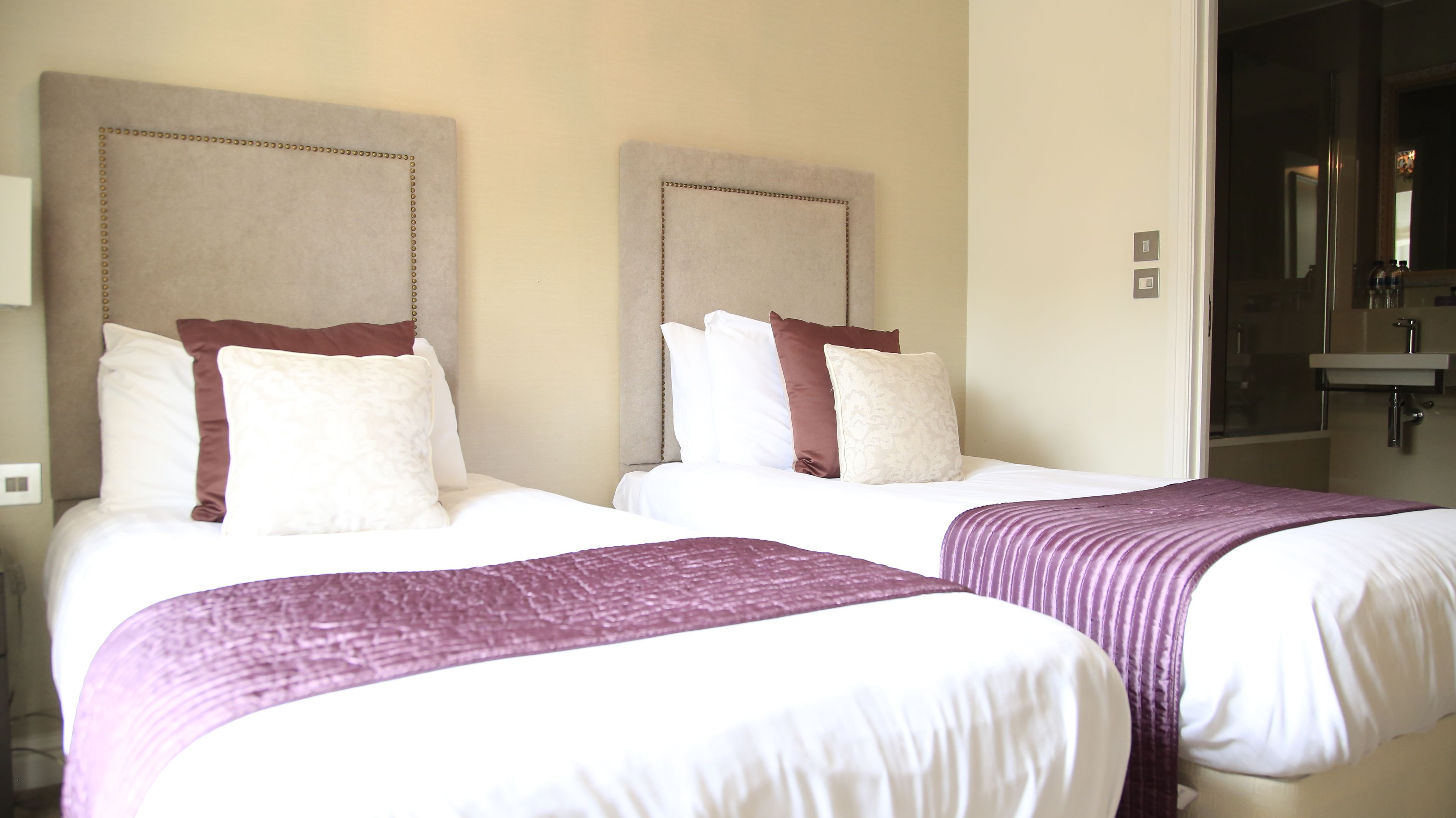 Two queen-sized beds with headboards, white bedding, and purple throw blankets.