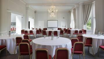 A large conference room with round tables and red chairs, a chandelier, and a projector screen.