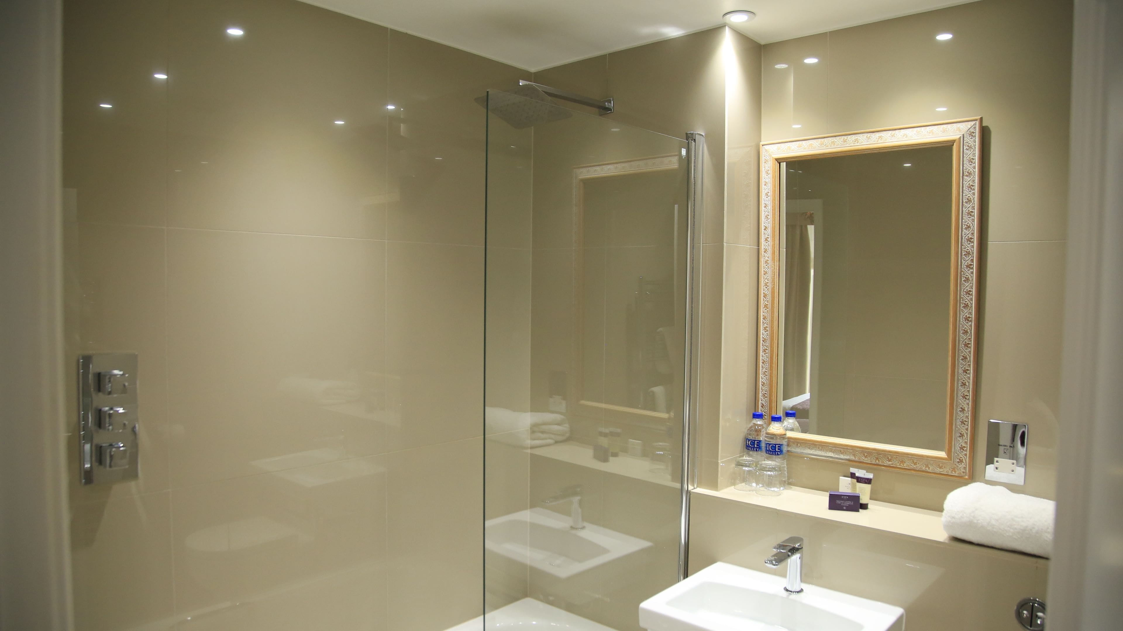 A modern bathroom with a glass shower enclosure, a sink, and a large mirror with a decorative frame.