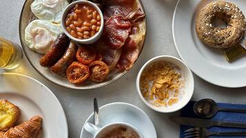Un desayuno con huevos, tocino, tomates, frijoles, salchichas, una dona, un tazón de cereal y una taza de café.