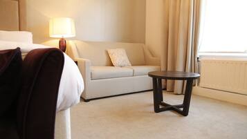 A hotel room with a bed, a sofa, a small table, a lamp, and a window with curtains.