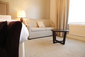 Relax in this serene hotel room featuring a comfortable bed, a sofa, and a large window with curtains.