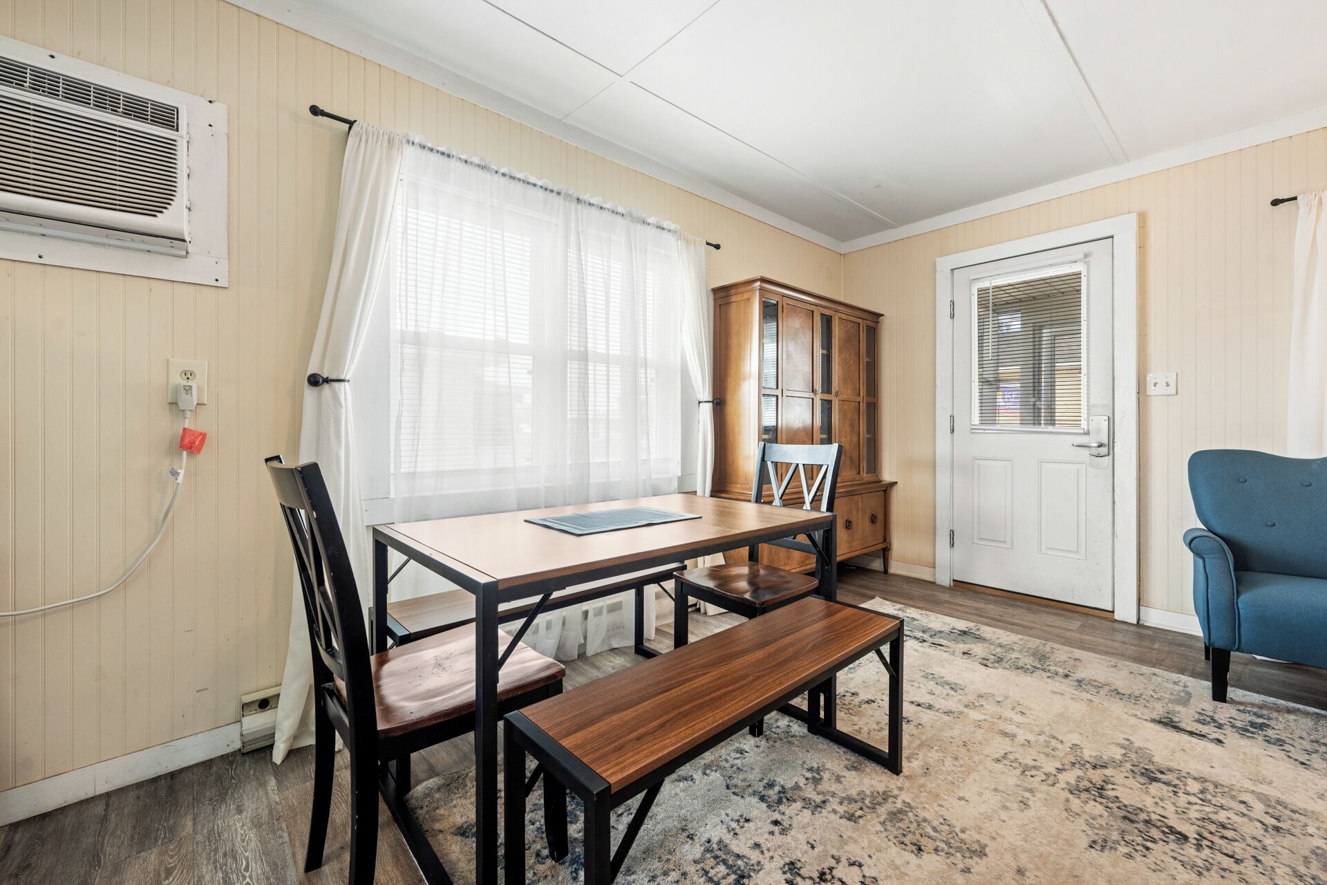 A room with a wooden table, two chairs, a bench, a cabinet, and a blue armchair.