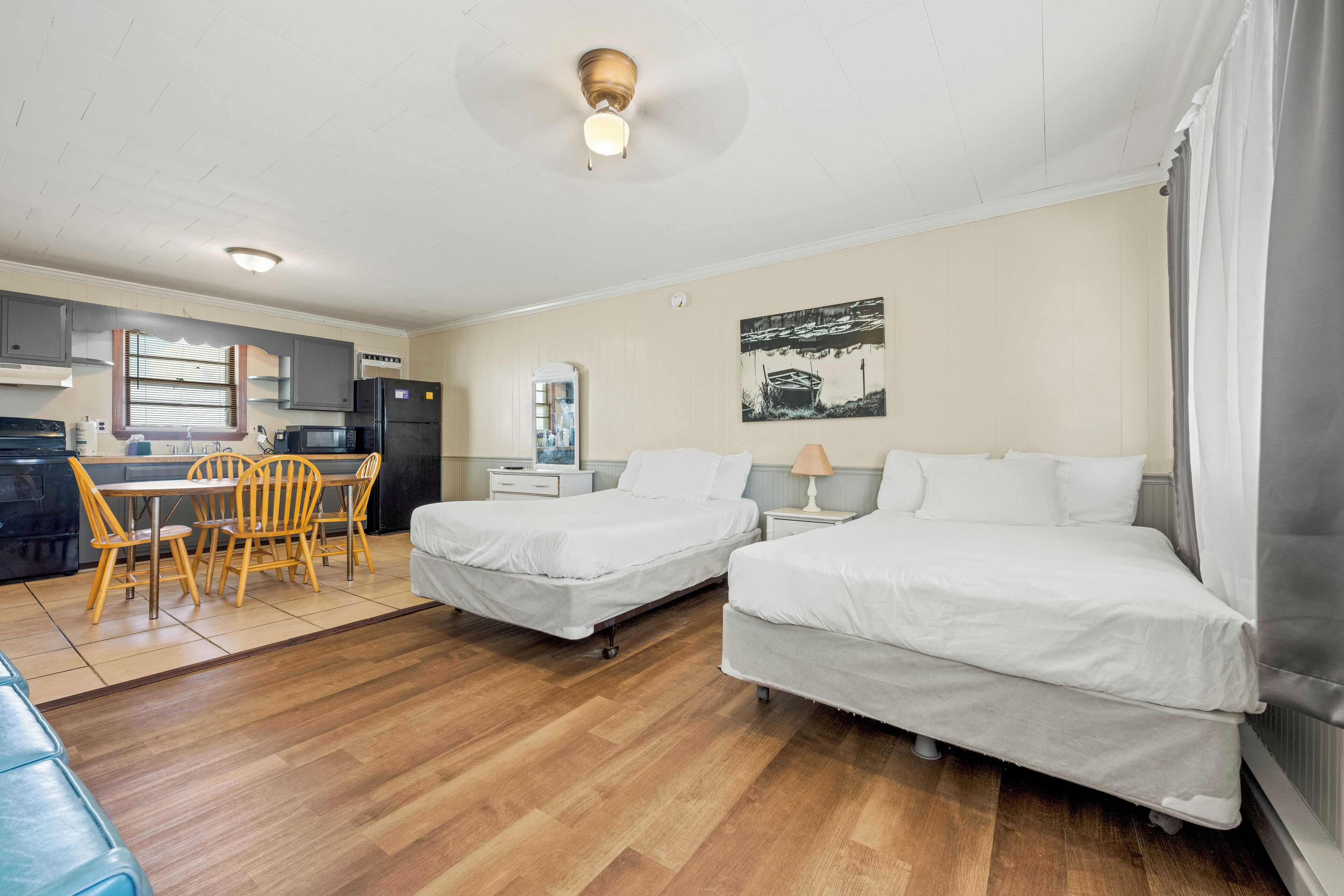 Une chambre d’hôtel avec deux lits, une table à manger avec des chaises, un coin cuisine et un ventilateur de plafond.