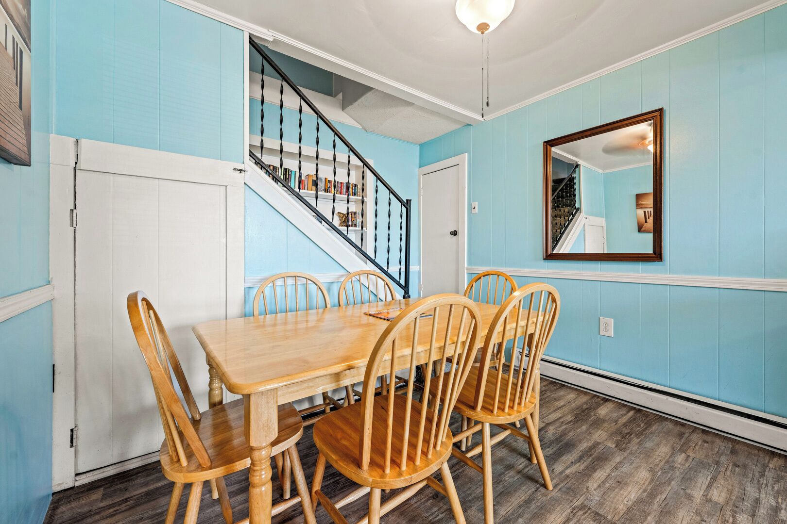 A dining area with a wooden table and chairs, a staircase, and a mirror on the wall.