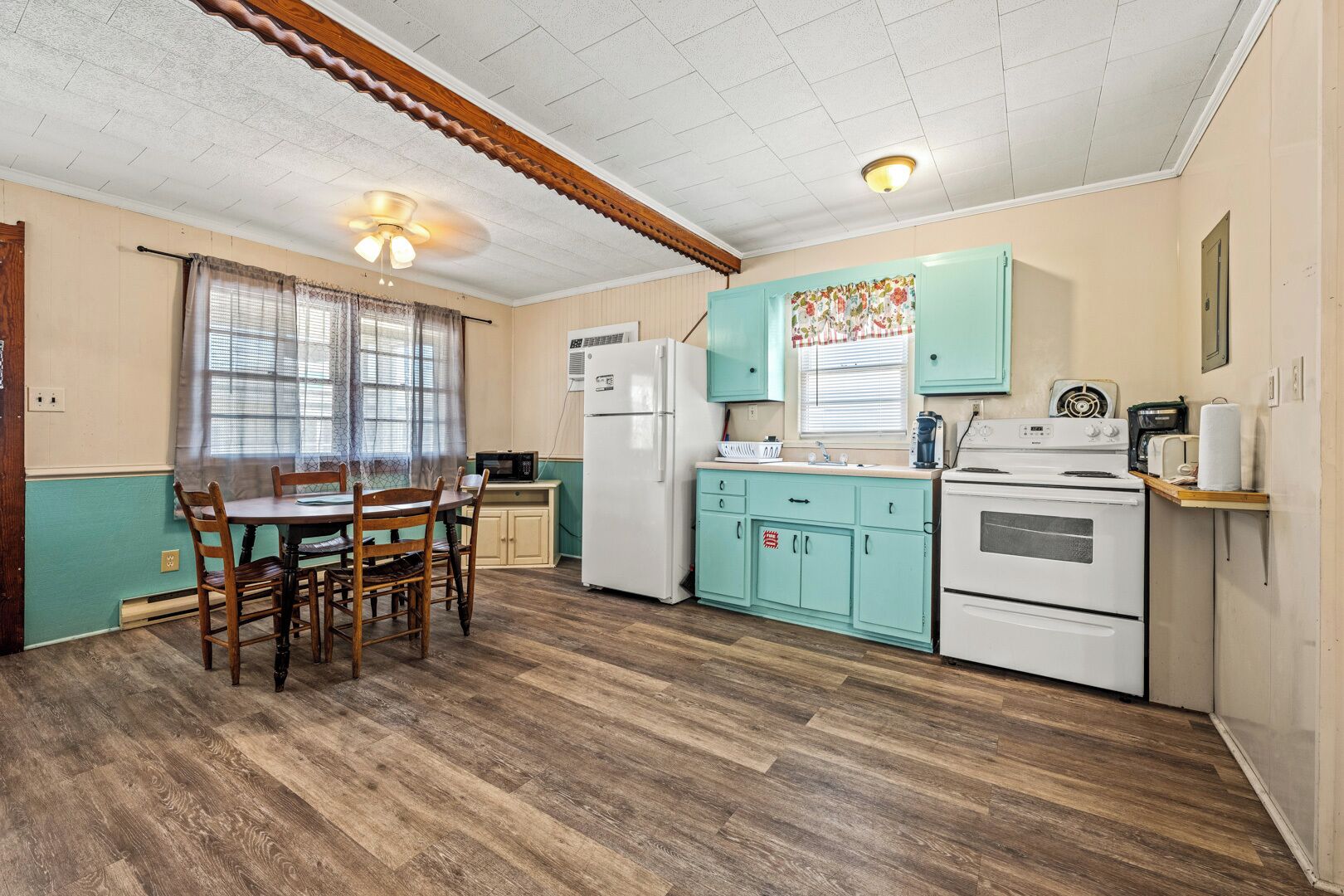A compact kitchen with a dining area, wooden flooring, and teal cabinetry.