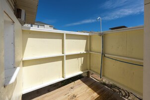 Un patio trasero cercado con una terraza de madera y una manguera para regar las plantas.
