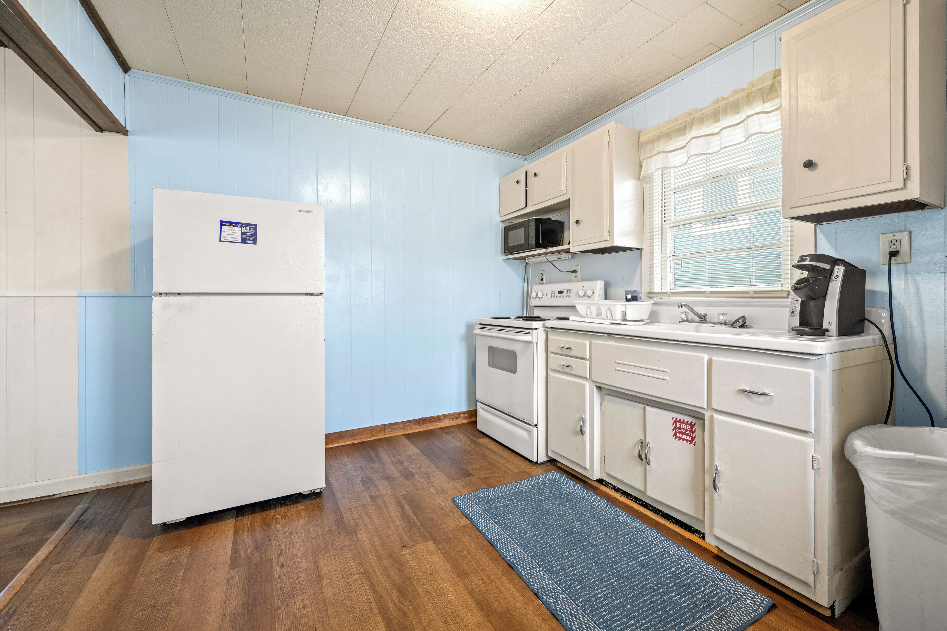 A compact kitchen with white appliances, a microwave, a stove, and cabinets.