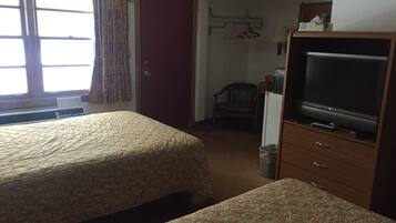 A hotel room with two beds, a television, a chair, and a wardrobe.