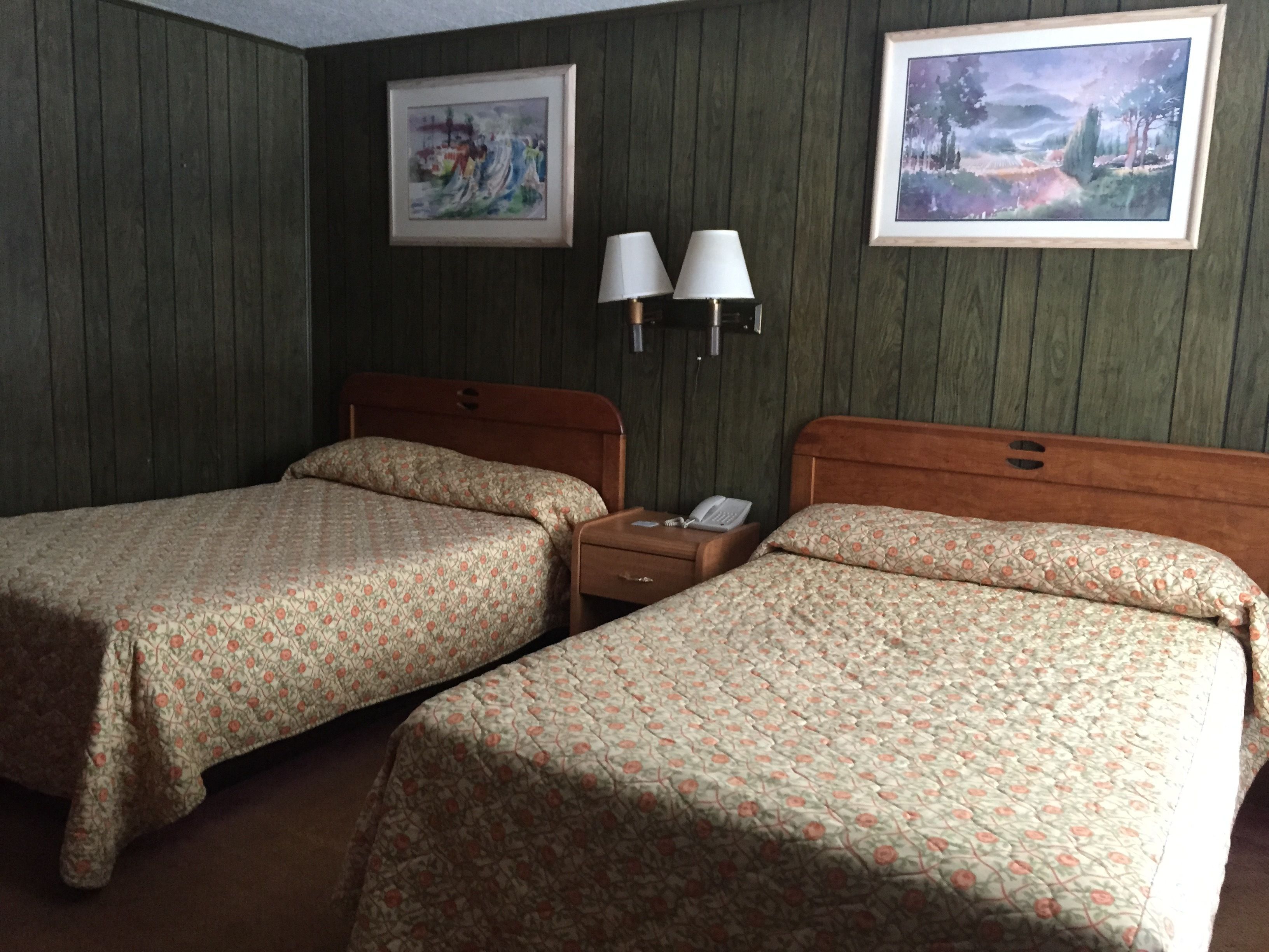 A hotel room with two beds, a nightstand, a lamp, and two framed pictures on the wall.