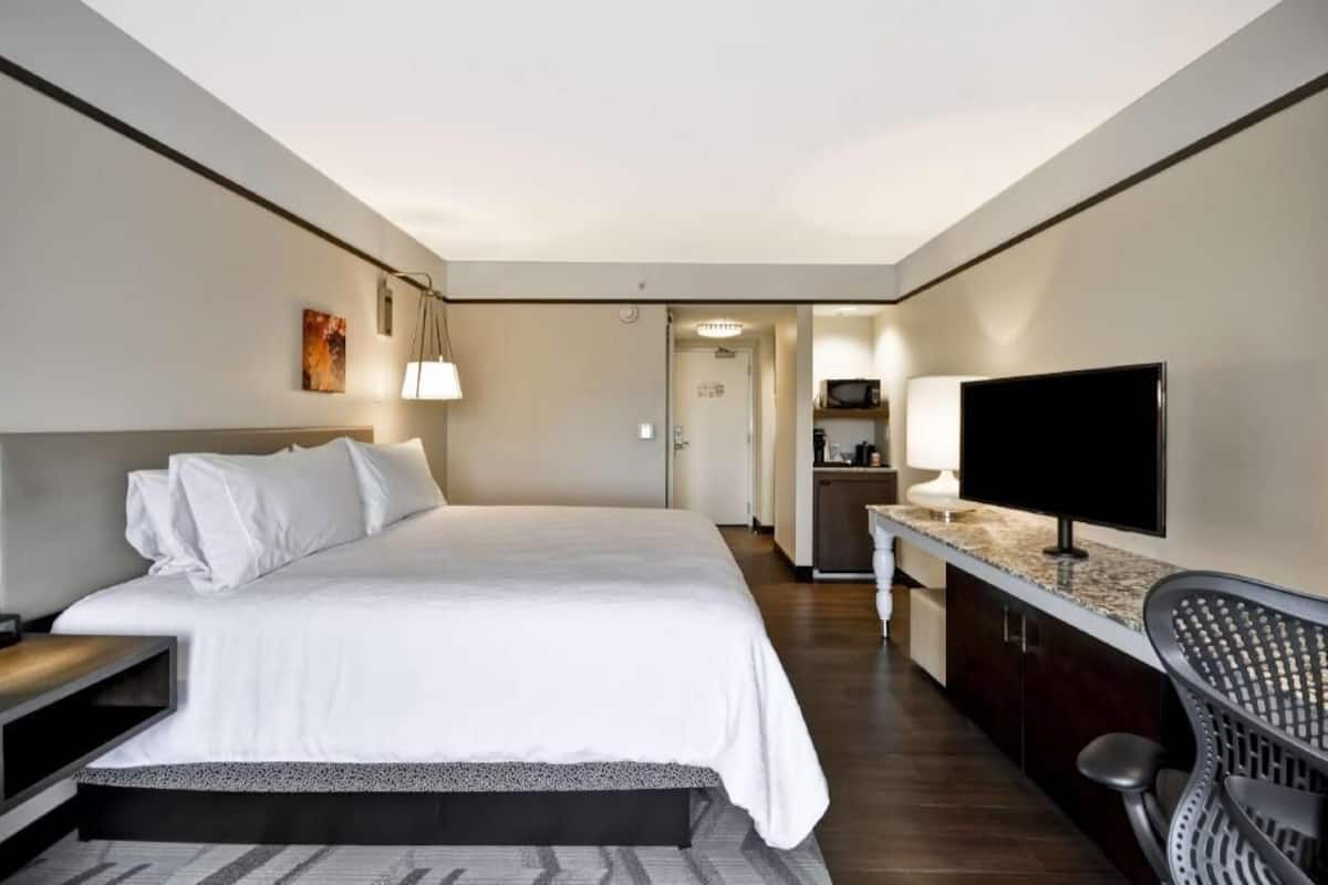 A hotel room with a bed, a TV, a desk, and a kitchenette.