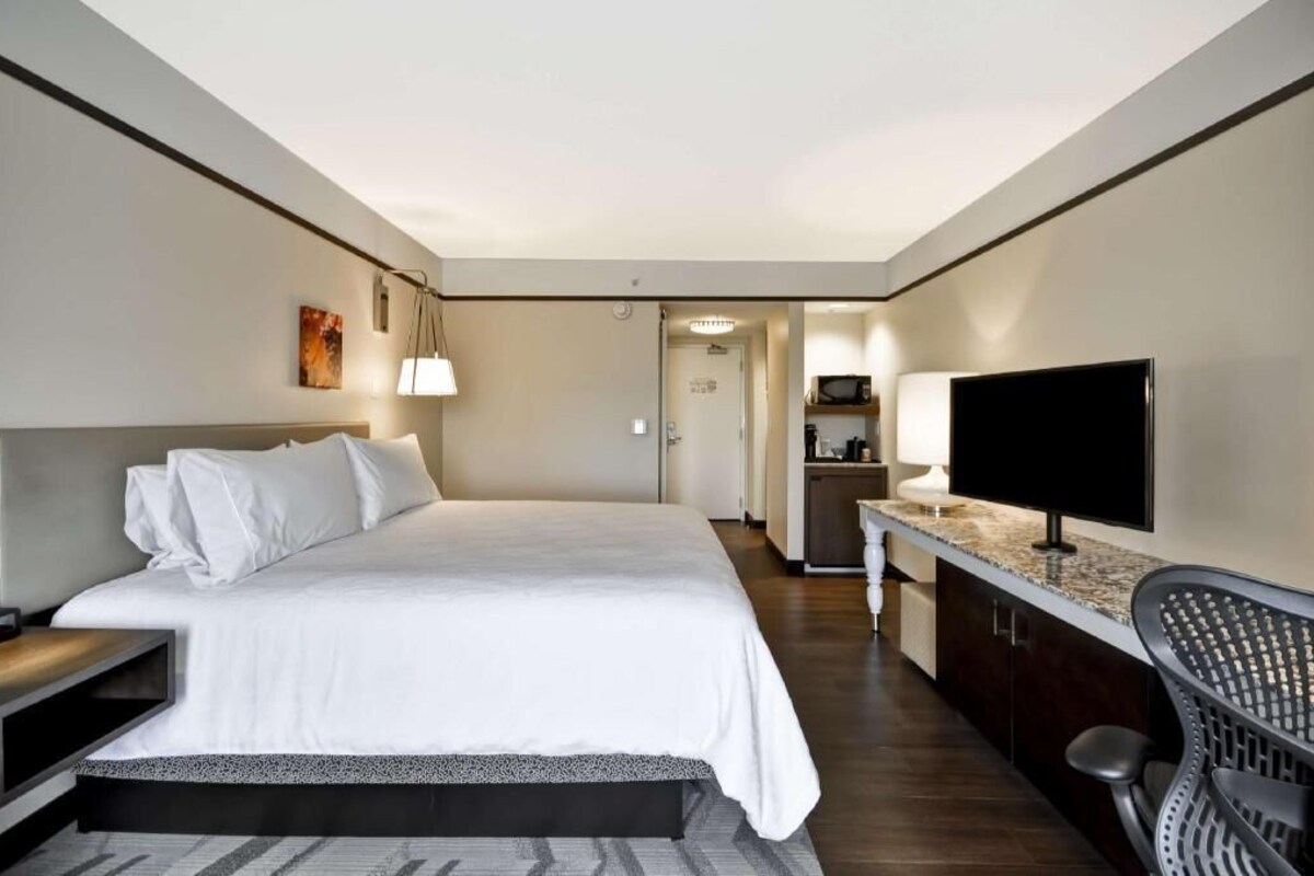 A hotel room with a bed, a TV, a desk, and a kitchenette.