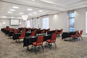 A conference room with multiple tables and chairs, a projector screen, and large windows. - Hilton Garden Inn Detroit Troy (Troy)