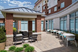 Une cour d’hôtel avec des espaces de repos en plein air, une terrasse couverte et une façade en briques.