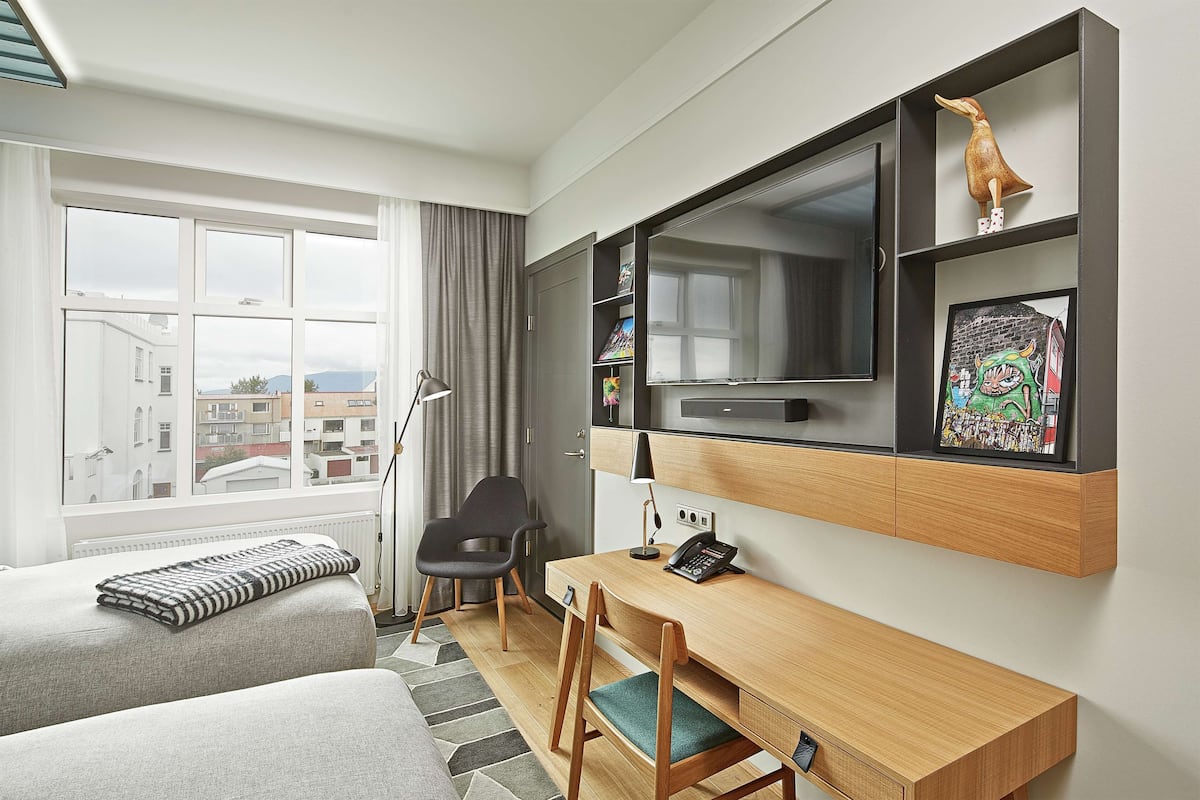 Een moderne hotelkamer met een groot raam, een bureau met stoel, een bed en een tv aan de muur.