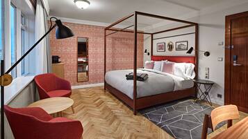 A modern bedroom with a four-poster bed, a red chair, a small round table, and a large window.