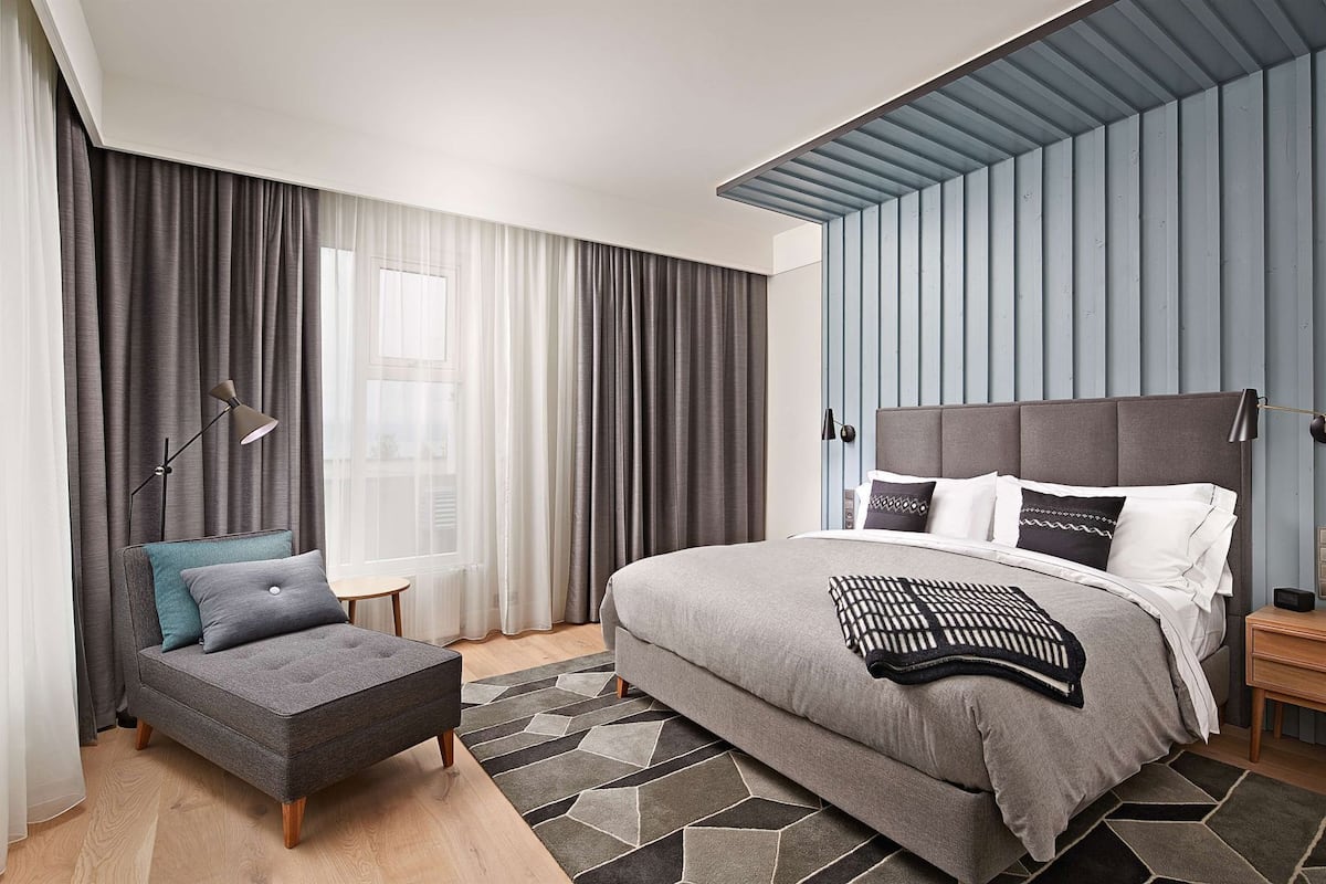 Een moderne slaapkamer met een groot bed, een kleine zithoek, een nachtkastje en een raam met gordijnen.