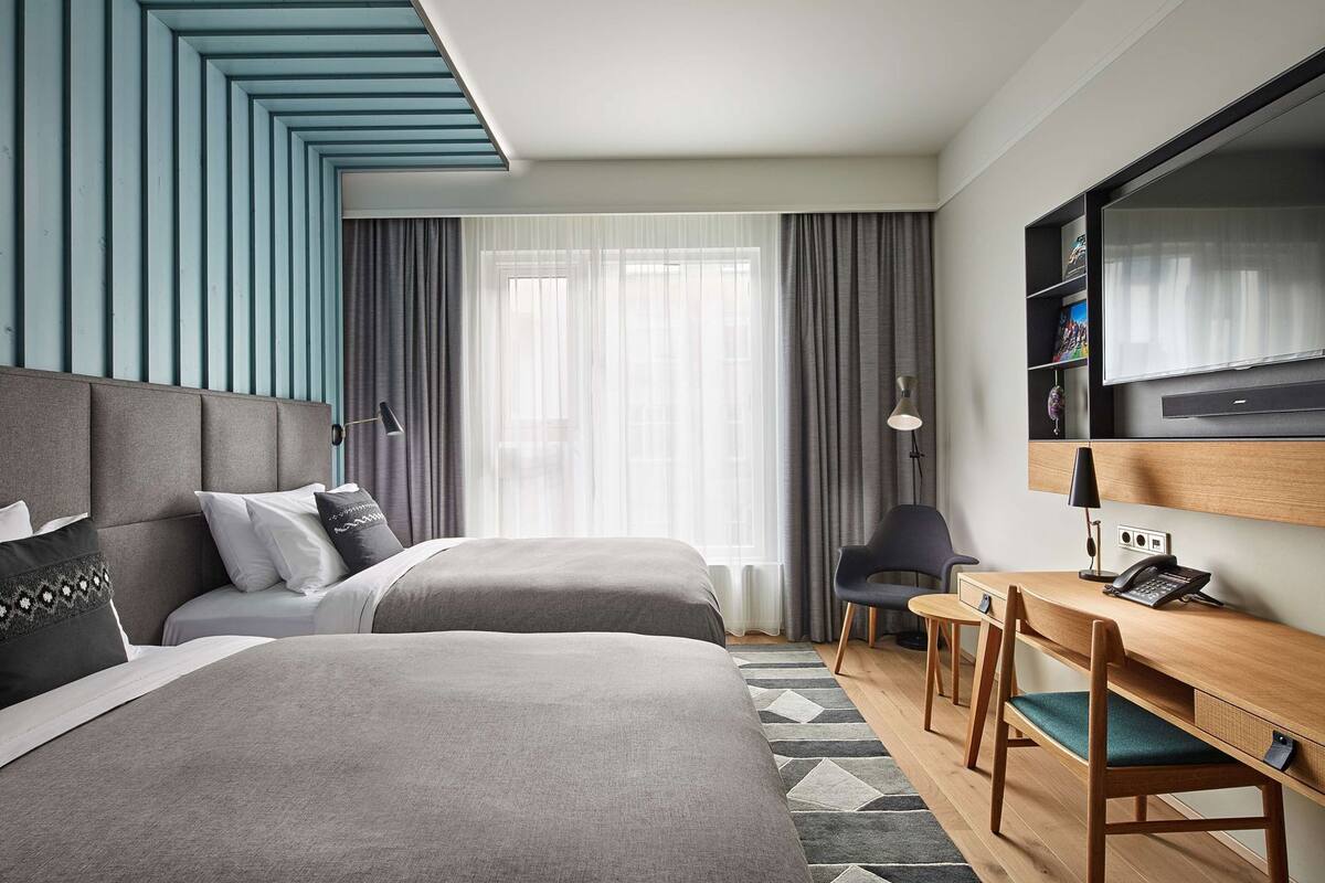 Een hotelkamer met twee bedden, een bureau, een stoel, een televisie en een groot raam met gordijnen.