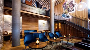 A modern lounge area with blue chairs, round tables, and a staircase. - Canopy by Hilton Reykjavik City Centre (Reykjavik)
