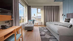 A hotel room with a bed, a desk with a chair, a small table, and a TV. - Canopy by Hilton Reykjavik City Centre (Reykjavik)