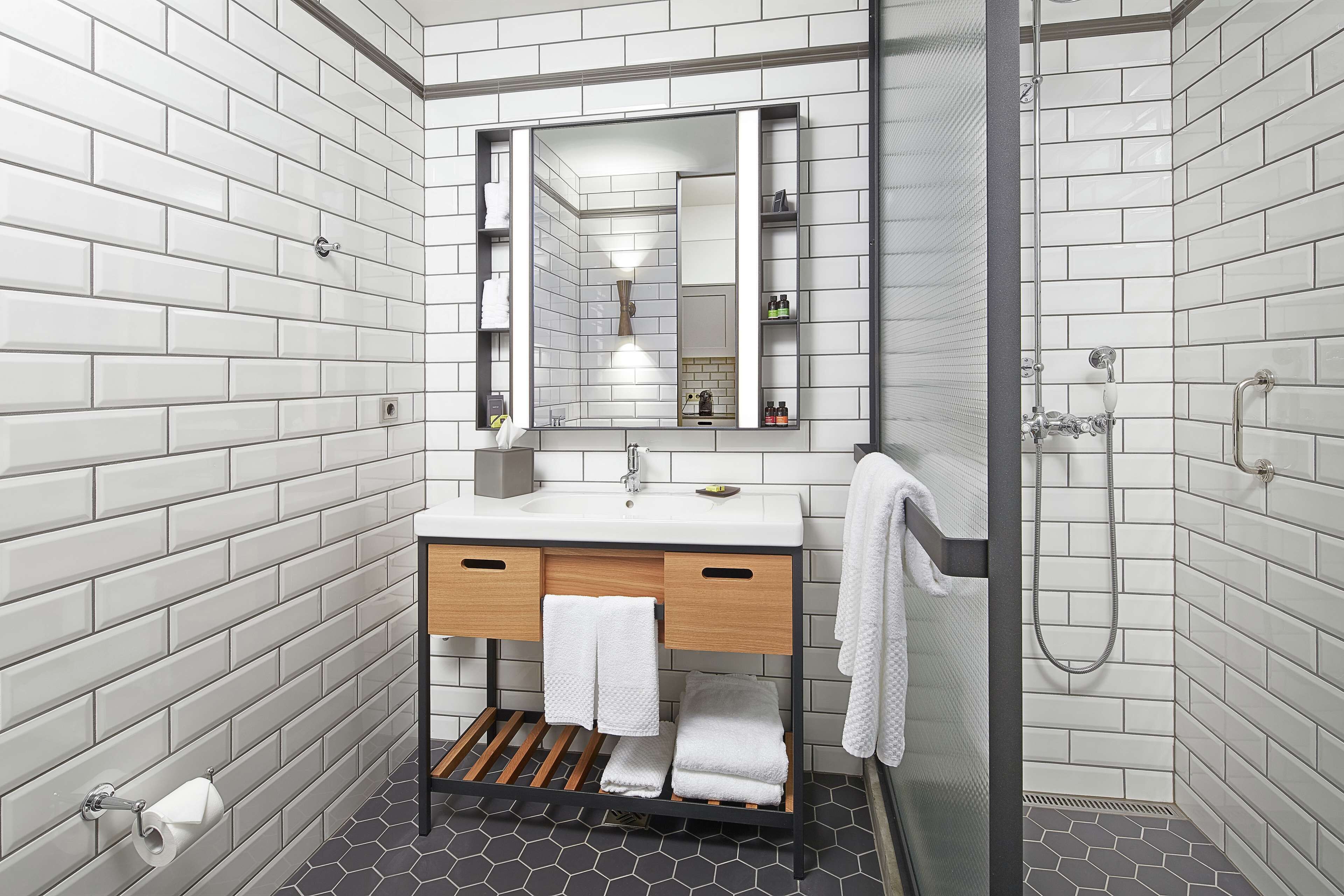 A modern bathroom with white subway tiles, a wooden vanity, a large mirror, and a shower area.