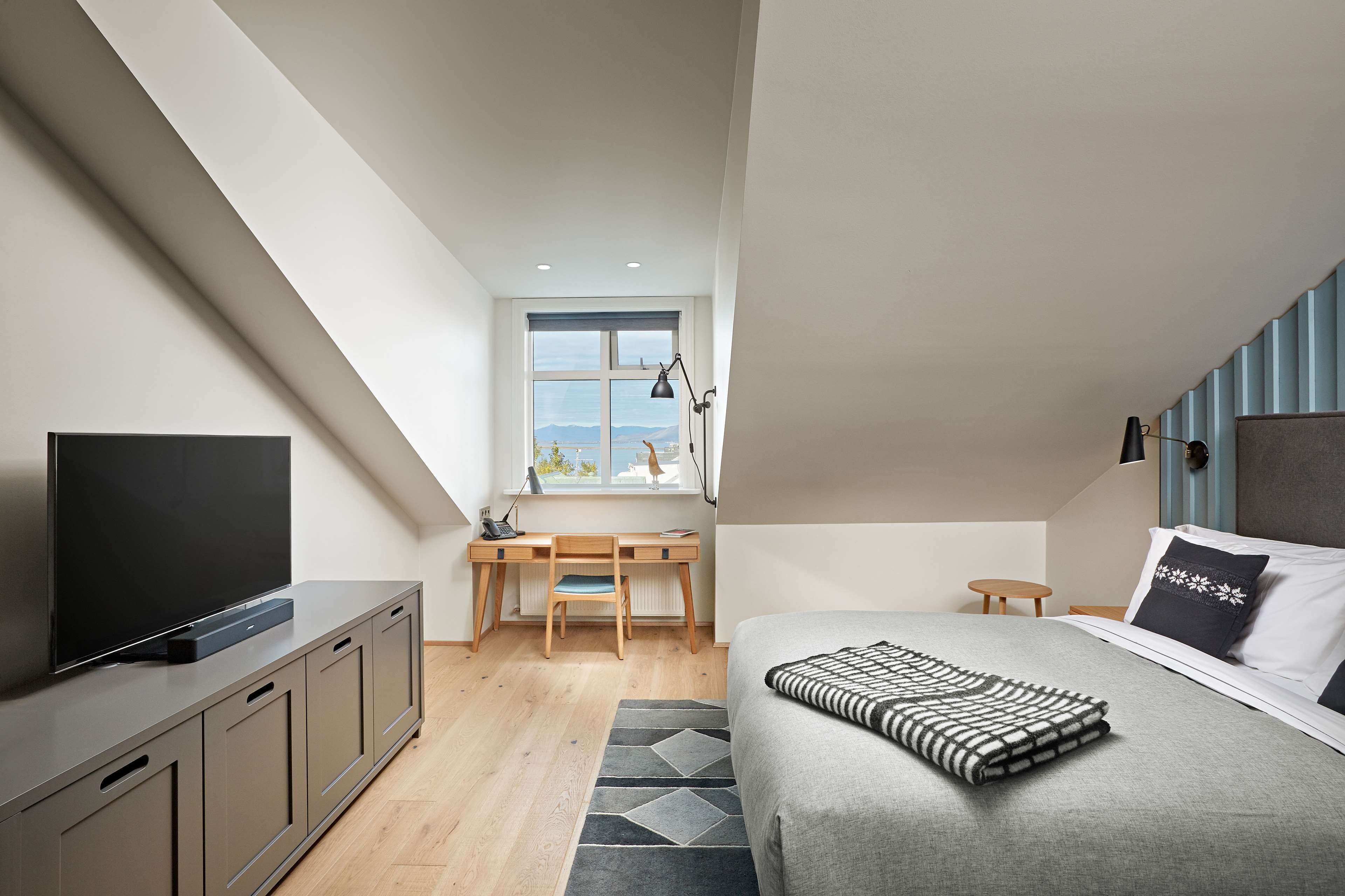 Un dormitorio moderno con una televisión de pantalla plana, una cama con una colcha estampada, un escritorio con una silla y una ventana con vistas.