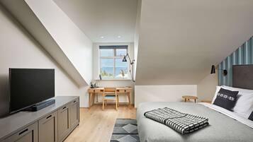 Un dormitorio moderno con una televisión de pantalla plana, una cama con una colcha estampada, un escritorio con una silla y una ventana con vistas.