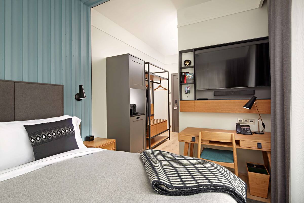 Een hotelkamer met een bed, een bureau, een kast, een televisie en een bedlampje.
