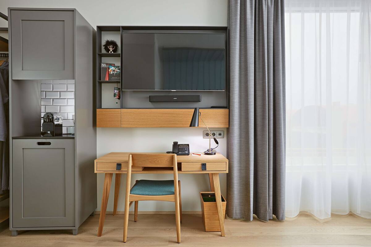 Een compacte, moderne kamer met een ingebouwd bureau, een televisie en een kleine kitchenette.