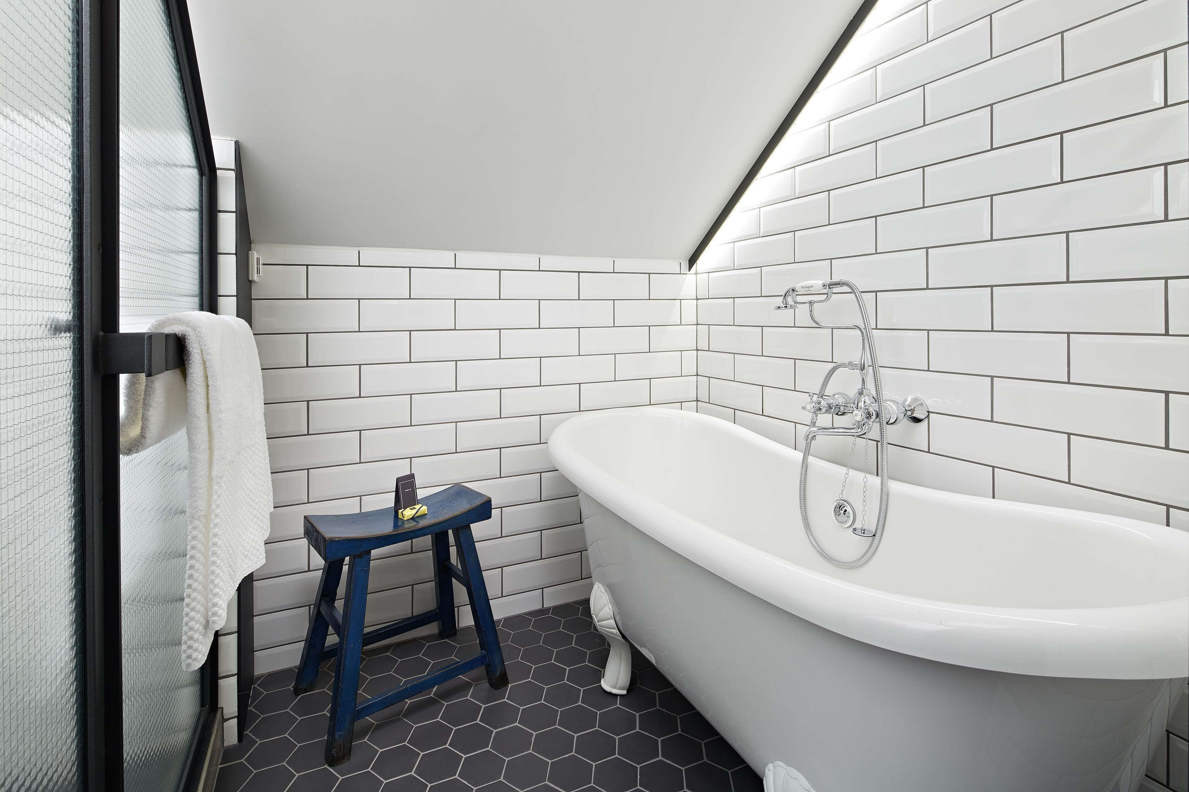 Une salle de bain avec une baignoire blanche, un tabouret bleu et une serviette blanche accrochée à une porte en verre.