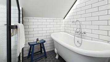 Une salle de bain avec une baignoire blanche, un tabouret bleu et une serviette blanche accrochée à une porte en verre.