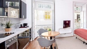 A compact kitchen with modern appliances, a dining area with two chairs and a small table, and a balcony with a white door and window. - Martinhal Lisbon Chiado (Lisbon)