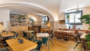 A cozy restaurant with wooden tables and chairs, a bar area with shelves of bottles, and large windows allowing natural light. - Martinhal Lisbon Chiado (Lisbon)
