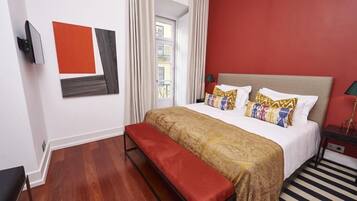 Een hotelkamer met een bed, een bankje, een televisie en een raam met gordijnen.