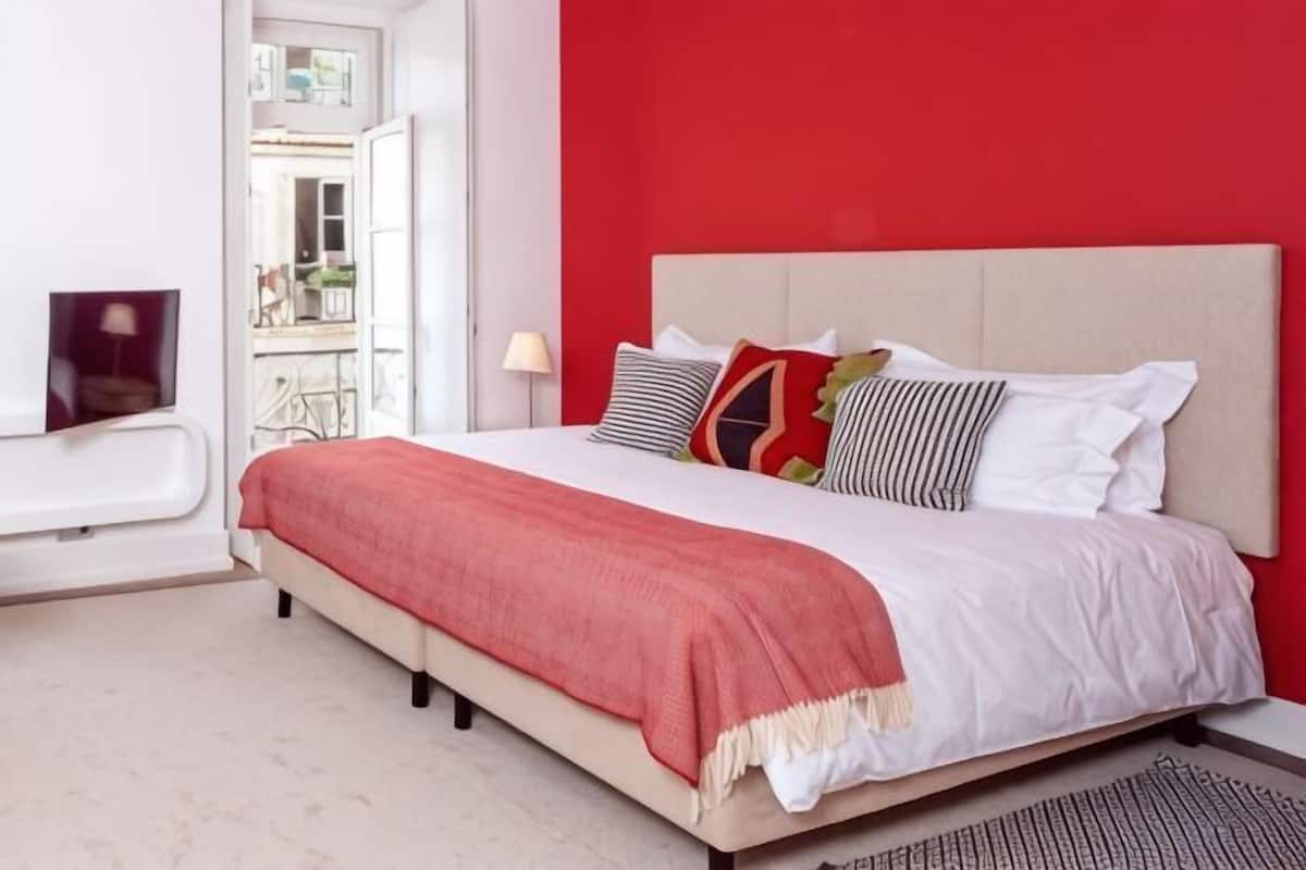 A bed with a red wall, a white headboard, and a red throw blanket.