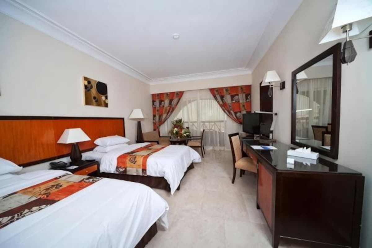A hotel room with two beds, a desk, a chair, a television, and a large mirror.