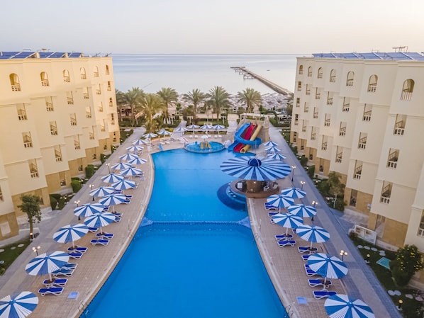 A resort pool with a water slide, sun loungers, and umbrellas.