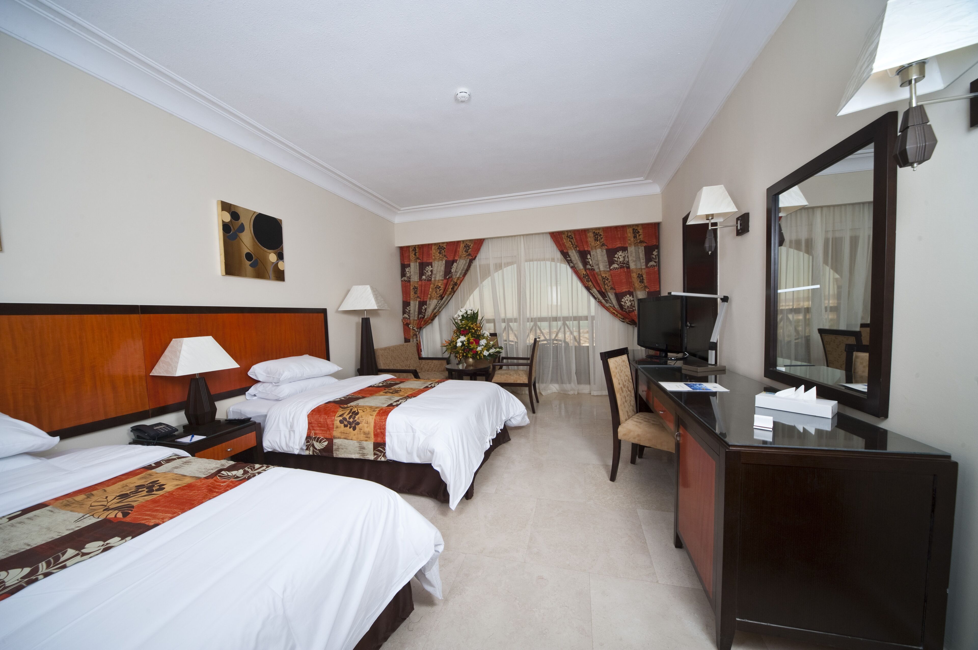 A hotel room with two beds, a desk, a chair, a television, and a mirror.